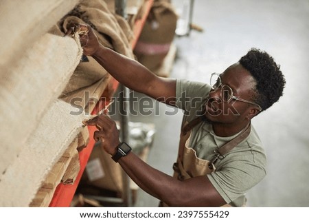 High angle portrait of Black young man reaching for coffee bags in warehouse at coffee roastery