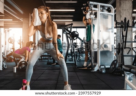 Tired athletic woman wiping sweat with a towel while taking a break at the gym. Exhausted and demotivated female standing in the fitness center.