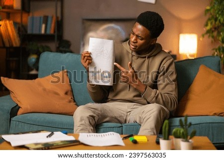 Curious young african american dark skinned man guy student sitting in the living room studying. Happy blogger vloger talking with his audience on Youtube channel explaining graphics and ecomomic