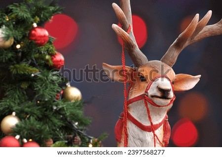 Christmas reindeer with rope to pull a sleigh, Christmas pine tree and background with blurred Christmas lights