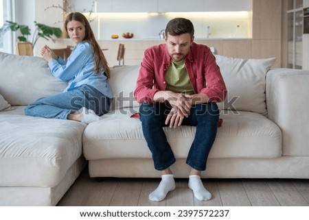 Gloomy upset passive man sitting on sofa apathetically looking on floor with blank stare, and offended woman with reproaching face expression. Misunderstanding, confrontation, crisis in family life