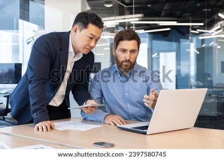 Two businessmen in suits work in the office, look at a laptop, discuss work issues, have a discussion. Royalty-Free Stock Photo #2397580745