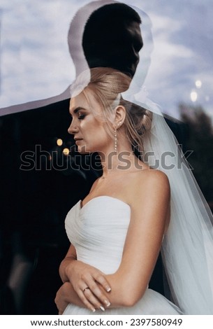 Beautiful bride near the window, reflection of the groom's silhouette. Wedding portrait of a cute blonde girl. Photography and concept.