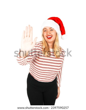 Cute young blonde woman doing a stop sign with her hand while wearing a Christmas Santa hat against a white background