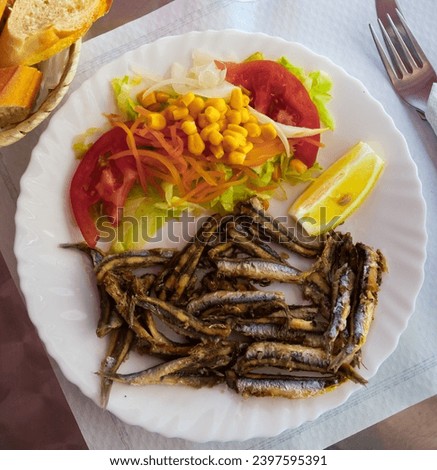 Picture of delicious dish of fried anchovy with tomatoes, corn and lemon..
