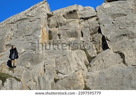 A chic girl, clad in black glamour, conquers Lucanian Dolomite peaks, disappearing amid imposing rocks—symbolizing audacious adventure in the wild.