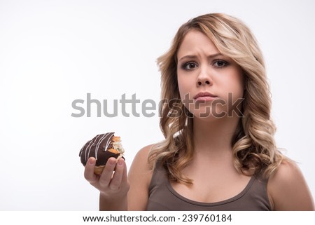 Half-length portrait of attractive worried blonde woman biting doughnut, weight loss concept, isolated on white background, selective focus