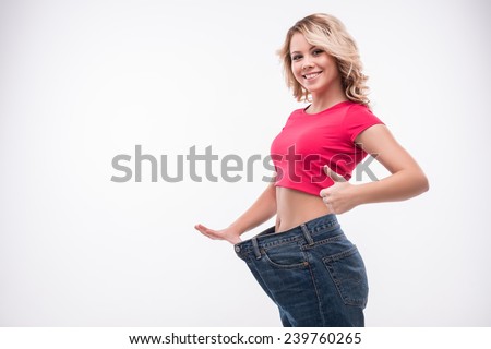 Full-length portrait of attractive slim young smiling woman in big jeans showing successful weight loss with her thumb up, isolated on white background Royalty-Free Stock Photo #239760265