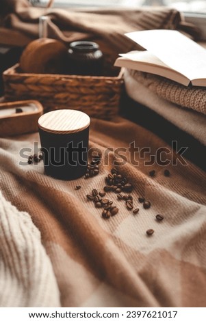 A burning candle with the smell of coffee, an open book and a stack of cozy sweaters, an aesthetic picture.