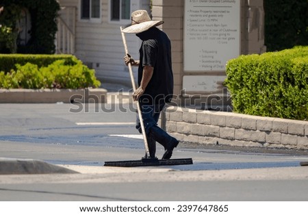 A man in a straw hat spreading new asphalt slurry  Royalty-Free Stock Photo #2397647865