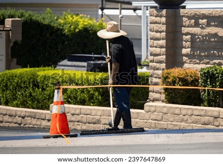 A man in a straw hat spreading new asphalt slurry  Royalty-Free Stock Photo #2397647869