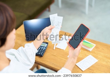 A woman holding a receipt and smartphone Royalty-Free Stock Photo #2397650837