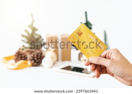 Woman's right hand holds golden credit card for online shopping on New Year's Day on background of Christmas tree, gift boxes, Christmas balls, pine cones and golden ribbon. There is a Clipping Path.
