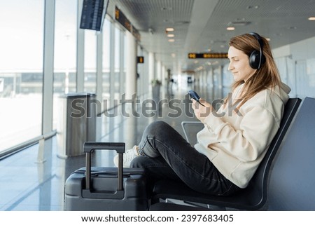 Woman use smartphone and earphones while waiting for her flight, student girl listening to music or podcast at the airport while waiting for a flight