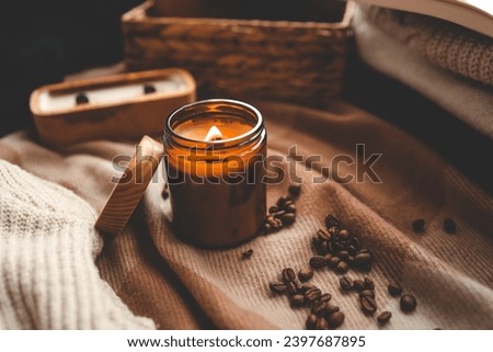 A burning candle with the smell of coffee, an open book and a stack of cozy sweaters, an aesthetic picture.