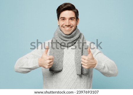 Young smiling happy ill sick man in gray sweater scarf show thumb up gesture isolated on plain blue background studio portrait. Healthy lifestyle disease virus treatment cold season recovery concept Royalty-Free Stock Photo #2397693107