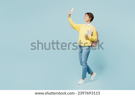 Full body side view young woman student wear casual clothes sweater backpack bag hold books do selfie shot mobile cell phone isolated on plain blue background. High school university college concept