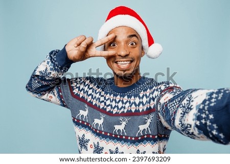 Close up young man wearing sweater Santa hat posing doing selfie shot pov on mobile cell phone show v-sign isolated on plain blue background. Happy New Year 2024 celebration Christmas holiday concept