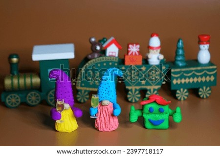 Two toy dwarfs made of plasticine with glasses of champagne on the background of a Christmas train. New Year's holidays and Christmas. Decorations and decorations.