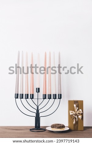 Black hannukia candlestick with nine multicolored candles and a chocolate donut on the white background. Celebration of Hanukkah concept