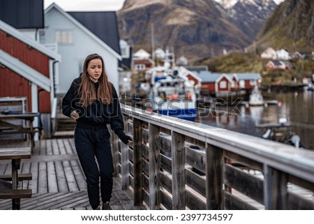 young woman dancing on a woden pond in typical nordic village with red houses on lofoten islands in norway
