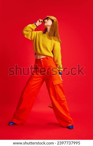 Full length portrait of attractive young lady dressed retro style bright outfit with sunglasses posing against vivid red background. Concept of human emotions, modern fashion, bright style trends.