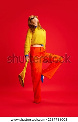 Creative portrait of funny girl, posing dressed bright retro fashion outfit with sunglasses, accessories against vivid red background. Concept of human emotions, modern fashion, bright life, trends.