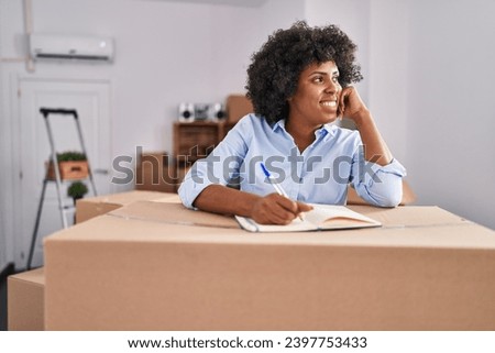 African american woman smiling confident writing on notebook at new home