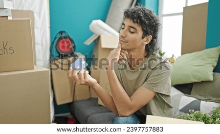 Young hispanic man holding credit card sitting on sofa thinking at new home