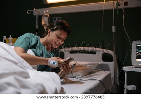 Young girl smiling holding the phone in her hands checking the latest news in the world while being treated in the hospital.