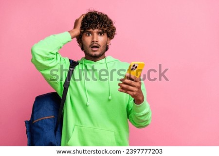 Photo of confused indian man with open mouth touching head hold smartphone wear rucksack forgot schedule isolated on pink color background