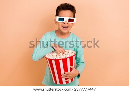 Photo of funky cheerful boy enjoy new movie 3d glasses eat popcorn big box isolated on beige color background