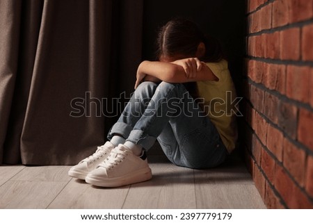 Child abuse. Upset little girl sitting on floor near brick wall indoors Royalty-Free Stock Photo #2397779179