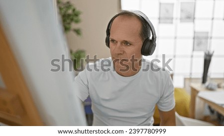 Confident middle aged man, an artist, sitting in his studio, engrossed in drawing with a brush on canvas, listening to music with headphones, immersed in his creative world