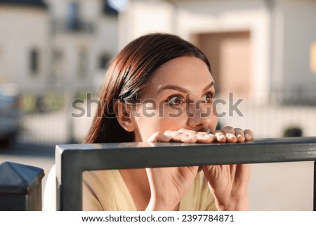 Concept of private life. Curious young woman spying on neighbours over fence outdoors Royalty-Free Stock Photo #2397784871