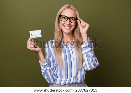 Photo portrait of blonde pretty young girl hold credit card touch specs dressed stylish striped outfit isolated on khaki color background