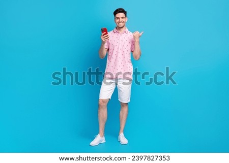 Full size portrait of attractive cheerful man hold smart phone direct finger empty space isolated on blue color background