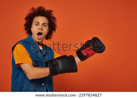 surprised sporty african american male model posing lively in boxing gloves on orange background