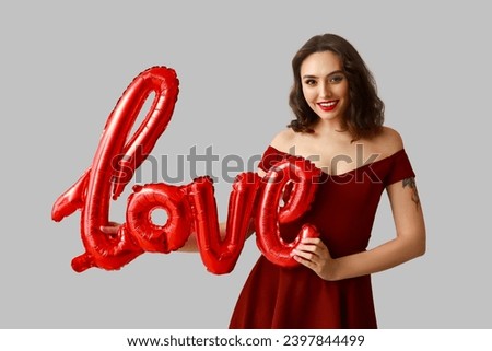 Beautiful young woman with air balloons in shape of word LOVE on grey background
