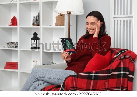 Happy young woman reading Christmas greeting card while sitting on armchair at home