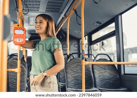 Female commuter holding handle and waves while standing in public transport. Beautiful woman enjoying trip at the public transport in the modern tram