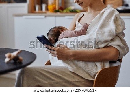 Cropped shot of woman with phone and newborn in white blanket resting after feeding, copy space Royalty-Free Stock Photo #2397846517