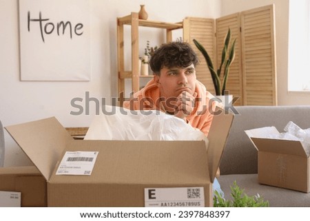 Thoughtful young man opening parcel at home