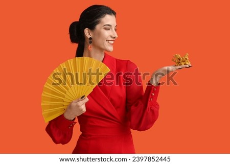 Beautiful young happy woman with golden dragon figurine and fan on orange background. Chinese New Year celebration