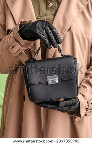 Woman in trench coat and leather gloves holding stylish handbag, closeup
