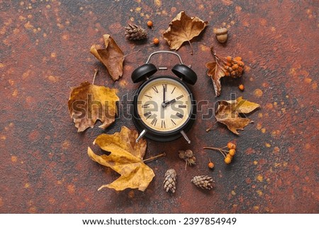 Alarm clock with viburnum and autumn leaves on grunge background