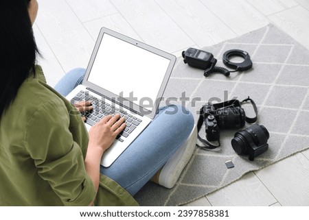 Female photographer with laptop and photo camera sitting on floor