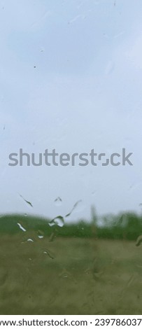 photo of raindrops splashing on a glass with a background of green grass and sky