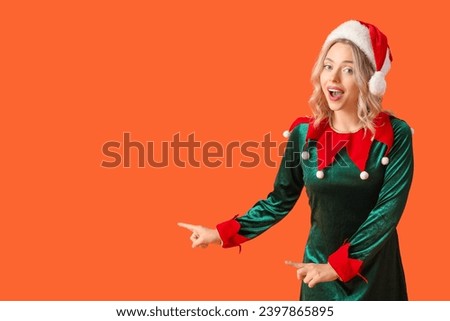 Happy young woman dressed as elf pointing at something on orange background