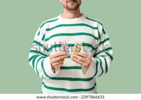 Sick young man with pills on green background, closeup